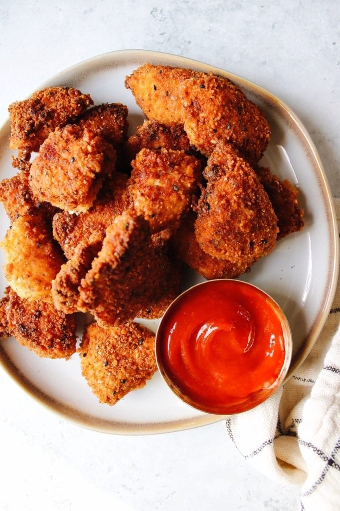 Cracker crusted chicken nuggets on a white plate with ketchup